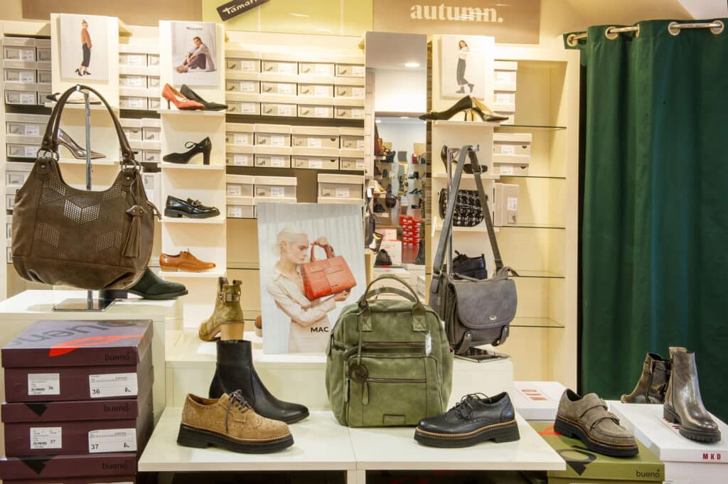 Vitrine de magasin de chaussures et sacs à main présentant des bottes, talons, sacs à dos et cabas Tamaris et Bueno pour l'automne.
